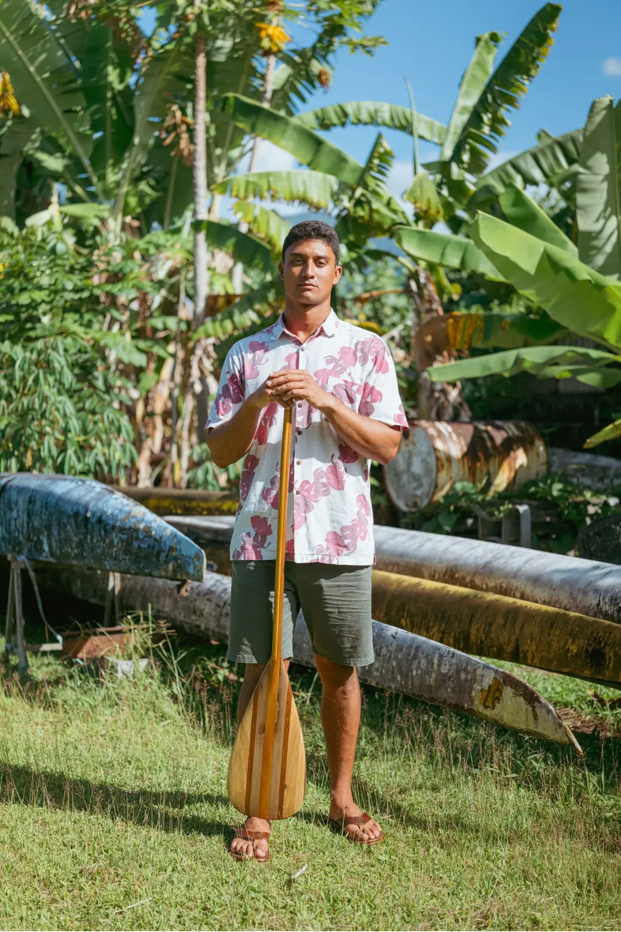 Hopena “Pena” Pokipala holding a wooden paddle beside outrigger canoe hulls