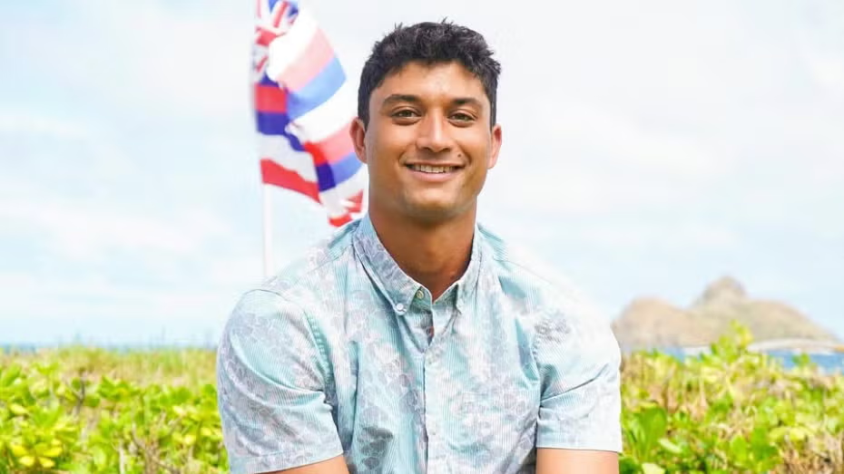 Portrait of Fullerton “Hopena” Pokipala smiling with the Hawaiian flag and Nā Mokulua behind him